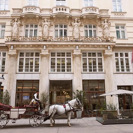 Steigenberger Hotel Herrenhof Відень Екстер'єр фото The photo shows the exterior of a grand hotel, featuring classical architecture with decorative statues and columns. In front of the hotel, there is a horse-drawn carriage with a driver. The hotel has large windows and elegant entrance doors, contrib