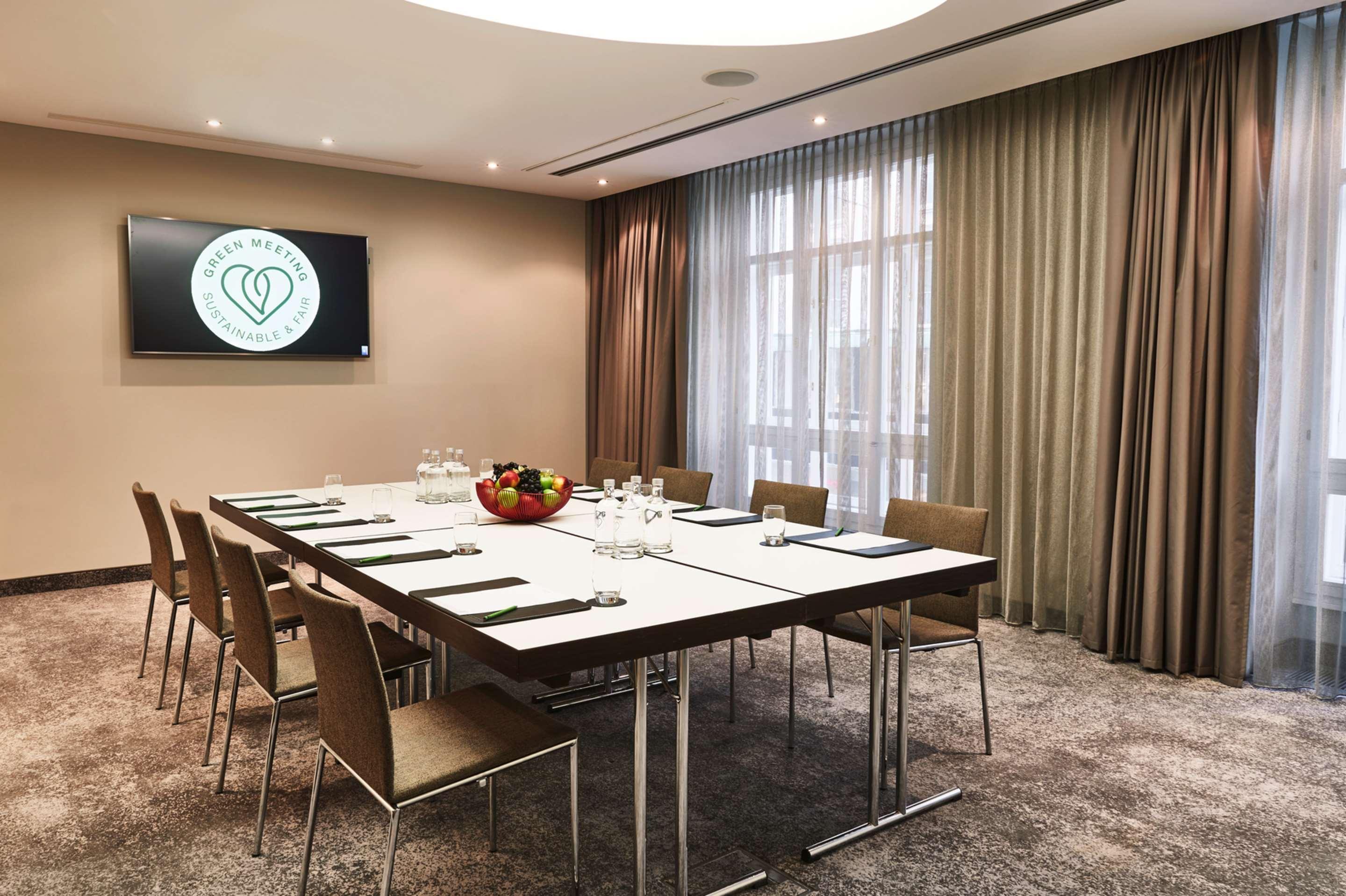 Steigenberger Hotel Herrenhof Відень Екстер'єр фото The photo shows a modern conference room set up for a meeting. In the center, there is a long rectangular table with several chairs arranged around it. The table is equipped with notepads and pens, and a bowl of fruit is placed in the middle. On the 