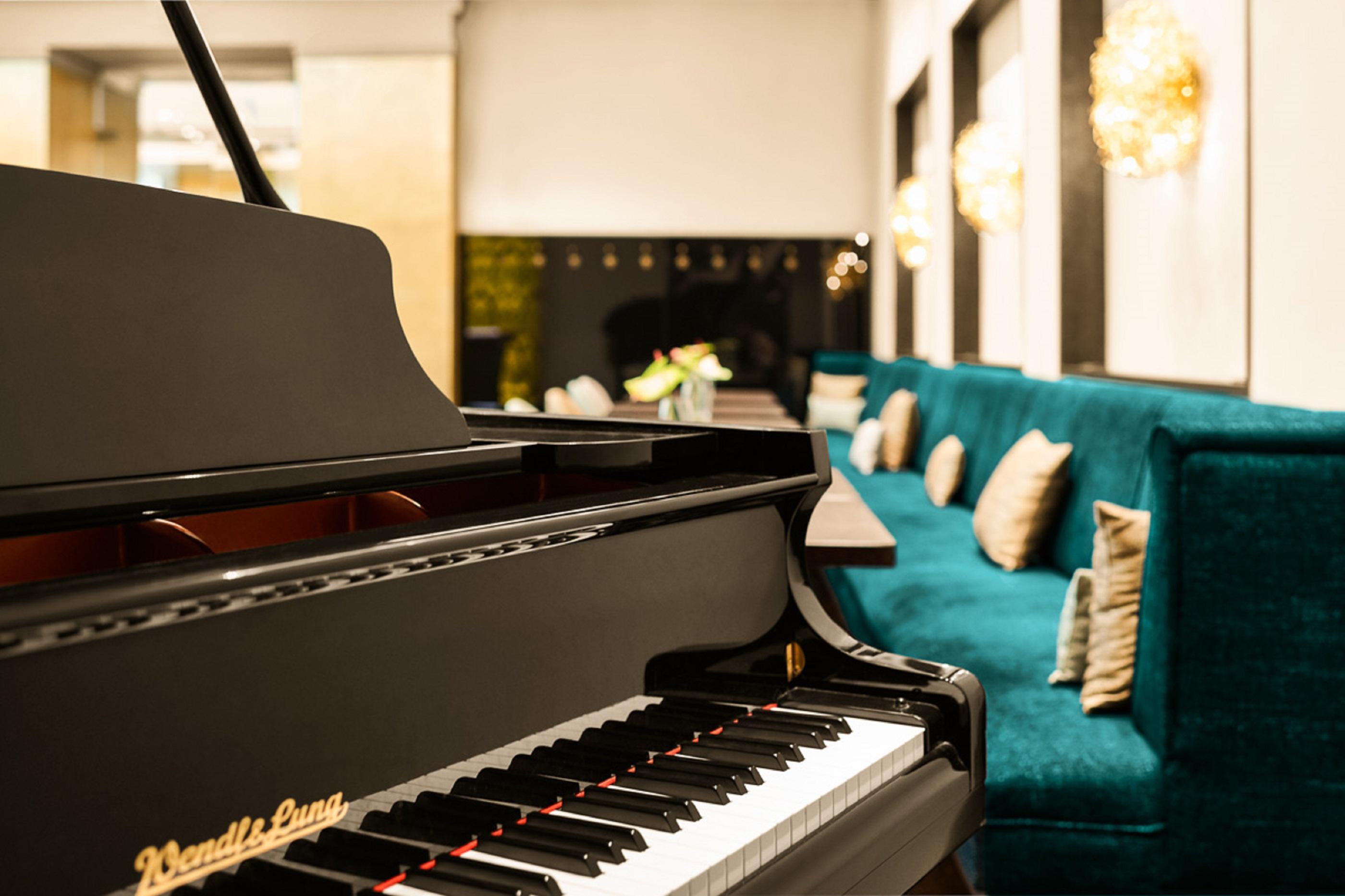 Steigenberger Hotel Herrenhof Відень Екстер'єр фото The photo features a close-up view of a grand piano, focusing on its keys and brand name, "Steinway & Sons." In the background, there is a stylish seating area with a vibrant teal couch adorned with decorative pillows. The setting appears modern and 