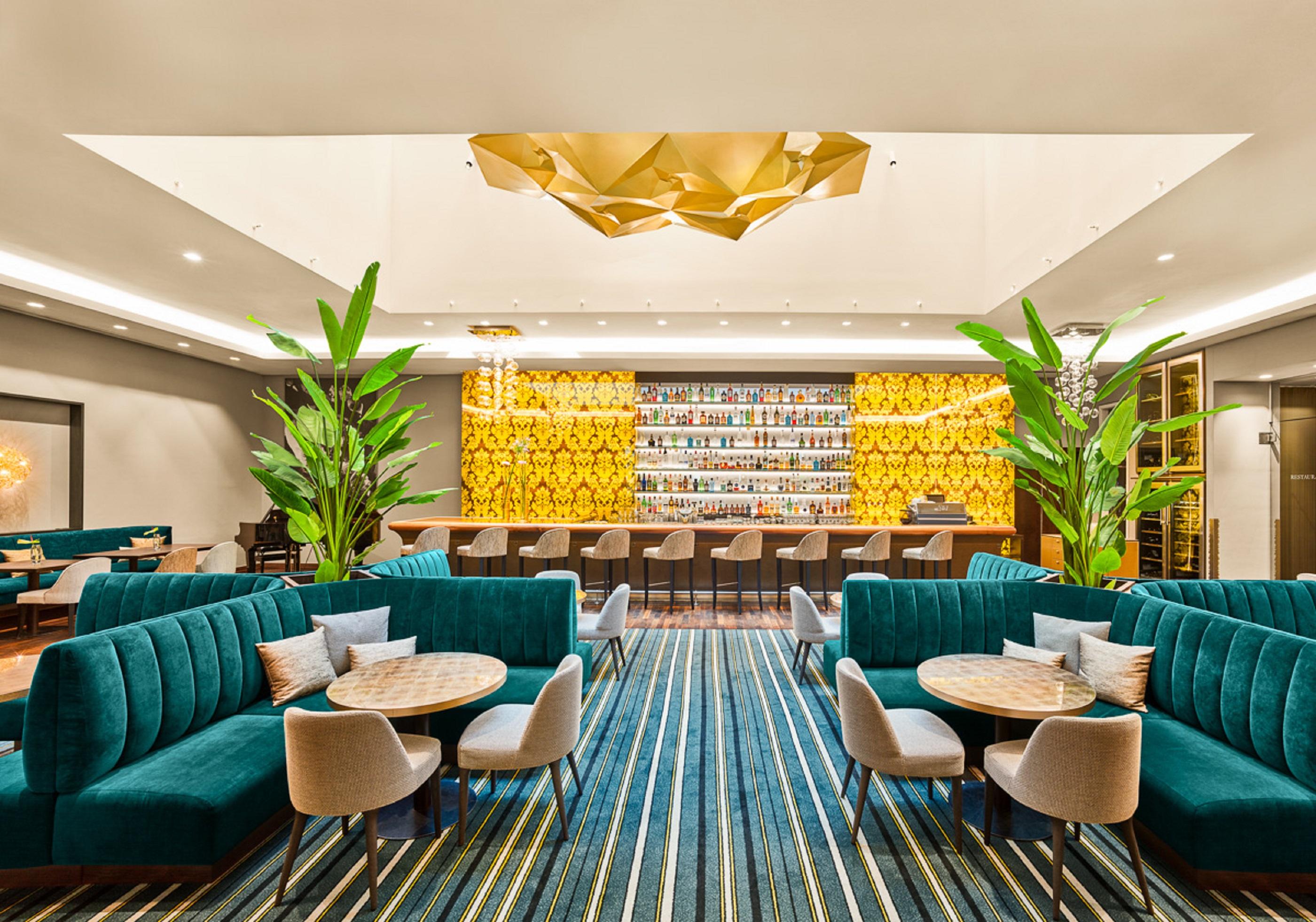 Steigenberger Hotel Herrenhof Відень Екстер'єр фото The photo shows a modern lounge or bar area featuring stylish teal seating arrangements, including plush sofas and round tables. In the background, there is a well-lit bar decorated with a vibrant yellow wall, adorned with various bottles. The space 