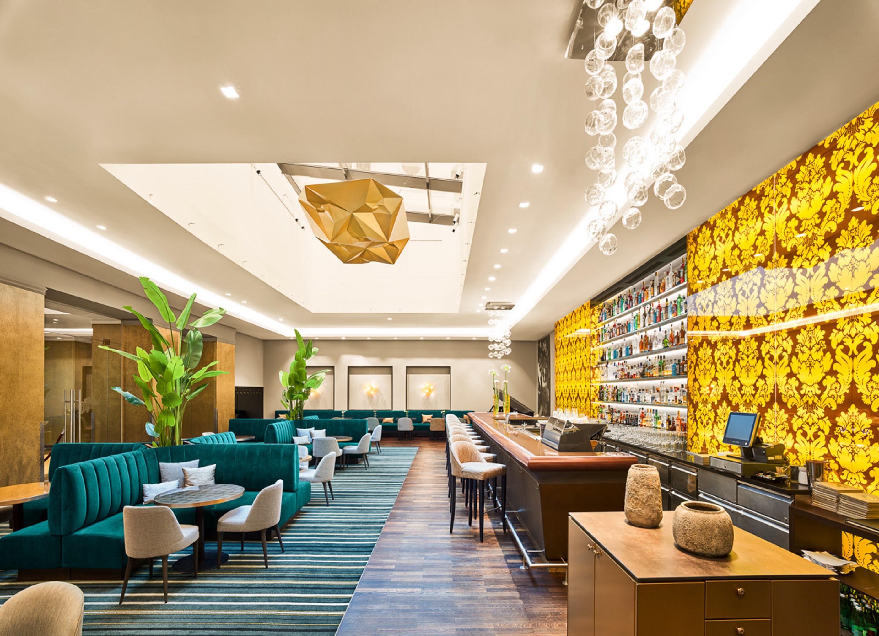 Steigenberger Hotel Herrenhof Відень Екстер'єр фото The photo shows a modern and stylish interior of a restaurant or lounge. The space features plush seating with teal upholstered sofas arranged around small white tables. The bar area is sleek, showcasing a variety of drinks displayed on a backlit she