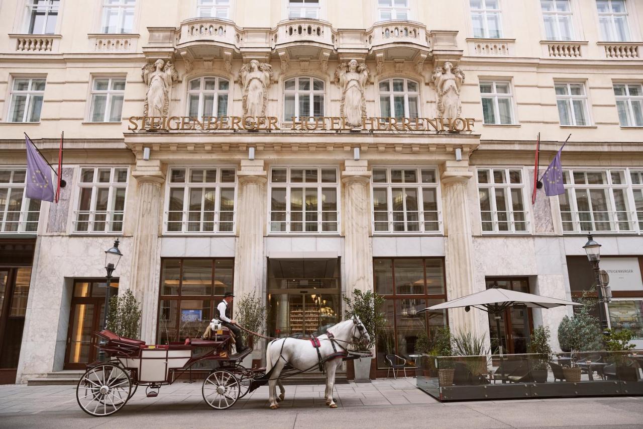 Steigenberger Hotel Herrenhof Відень Екстер'єр фото The photo shows the exterior of a grand hotel, featuring classical architecture with decorative statues and columns. In front of the hotel, there is a horse-drawn carriage with a driver. The hotel has large windows and elegant entrance doors, contrib