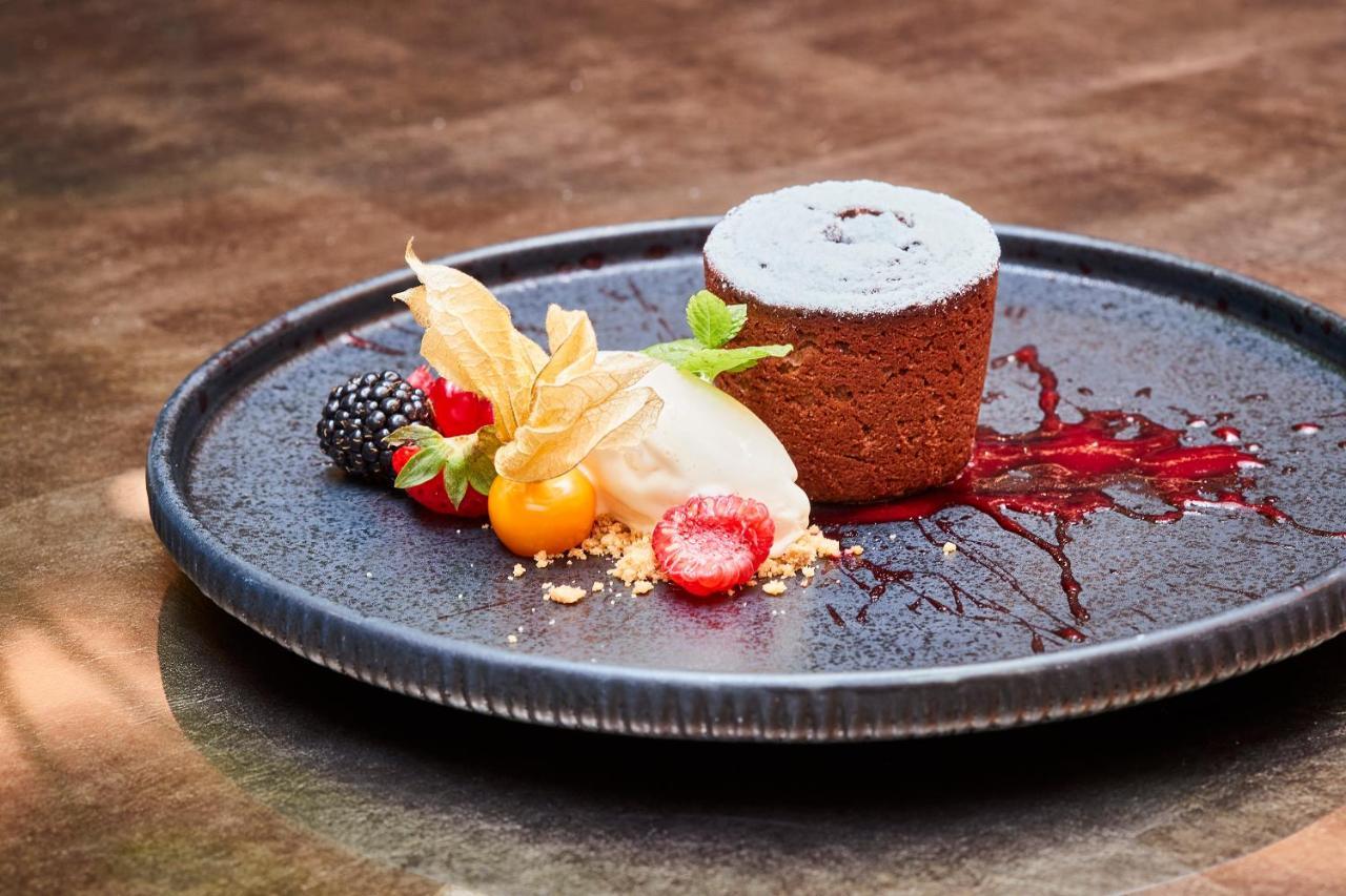Steigenberger Hotel Herrenhof Відень Екстер'єр фото The photo shows a beautifully presented dessert on a dark plate. It features a small, round chocolate cake, likely a molten or lava cake, dusted with powdered sugar. Beside the cake, there is a scoop of ice cream and a variety of colorful fruits, inc