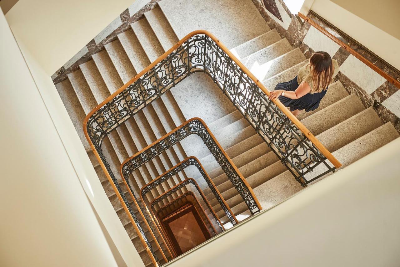 Steigenberger Hotel Herrenhof Відень Екстер'єр фото The photo shows a spiral staircase with multiple levels, featuring a beautiful railing with intricate designs. The stairs are made of light-colored stone, creating a clean and elegant appearance. In the lower part of the image, a person is seen walki
