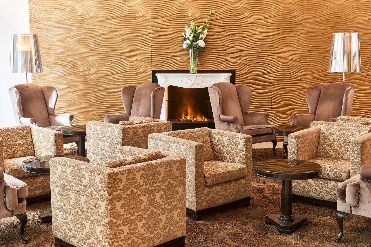 Steigenberger Hotel Herrenhof Відень Екстер'єр фото The photo depicts a cozy and elegantly designed lounge area. There are several upholstered armchairs and sofas arranged in a welcoming manner. The furniture features a light, floral pattern, and there are small tables beside the seating. A fireplace 