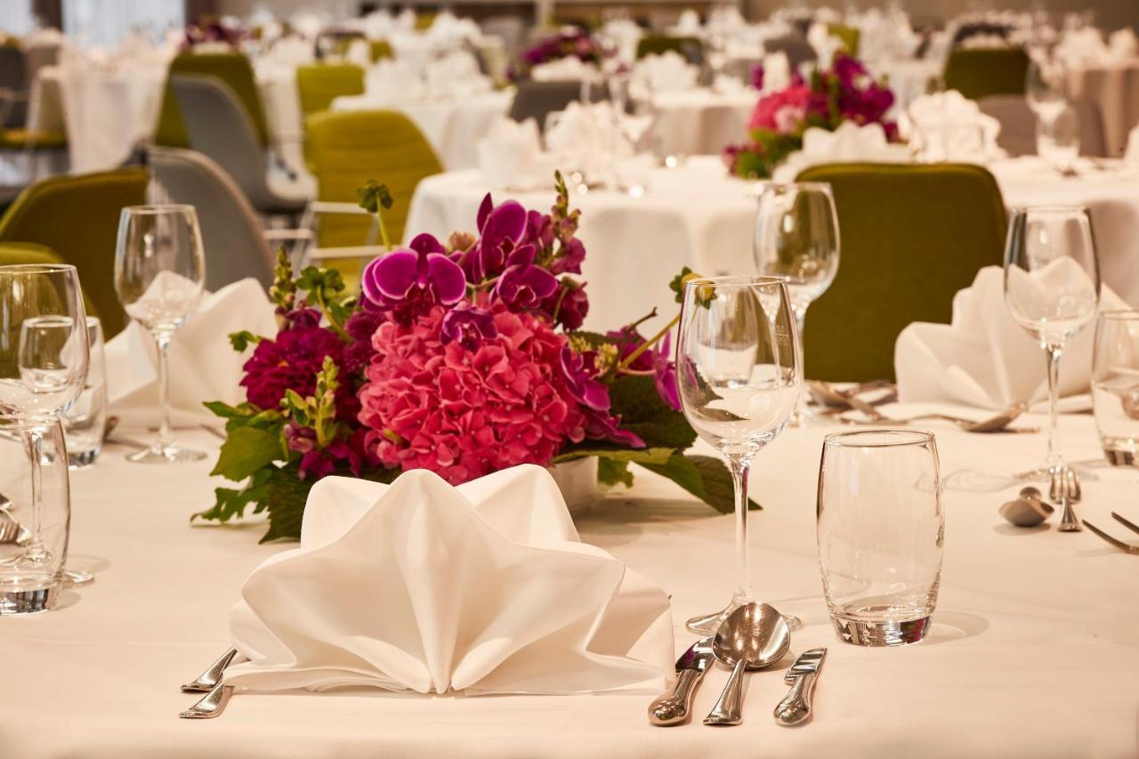 Steigenberger Hotel Herrenhof Відень Екстер'єр фото The photo depicts an elegantly set dining table with white tablecloths. Each setting includes neatly folded white napkins, wine glasses, and silverware arranged carefully. A decorative centerpiece features vibrant pink and purple flowers, creating a 