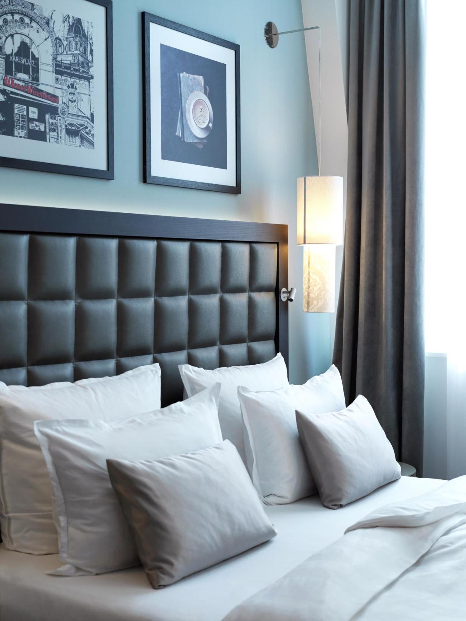 Steigenberger Hotel Herrenhof Відень Екстер'єр фото The photo shows a cozy bedroom setting. The headboard of the bed is upholstered in a dark material with a tufted design. There are several white pillows on the bed, adding to the comfort. The wall behind the bed has two framed pictures, and there is 