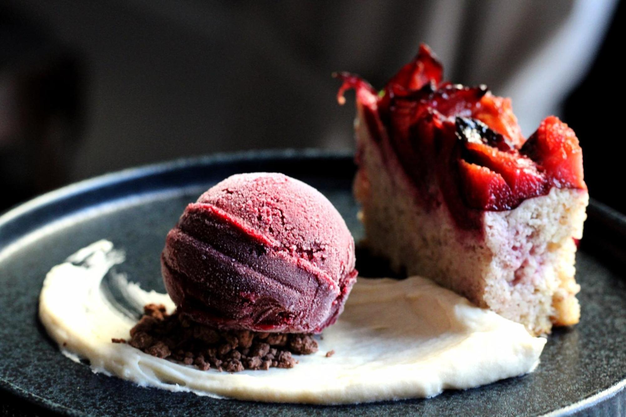 Steigenberger Hotel Herrenhof Відень Екстер'єр фото The photo shows a dessert plate featuring two main components. On the left, there is a scoop of purple ice cream, likely berry-flavored, sitting on a bed of cream or sauce. On the right, there is a slice of cake topped with a glossy fruit glaze, poss